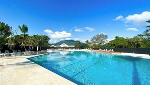 A large, clear swimming pool with lounge chairs and palm trees around it.