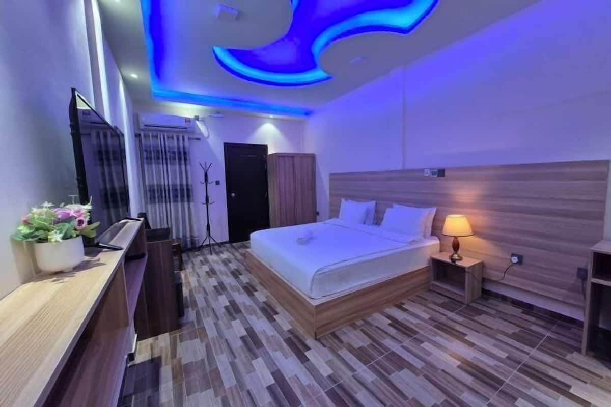 Une chambre d’hôtel moderne équipée d’un lit, d’une table de chevet, d’une lampe et d’un bureau avec une chaise.