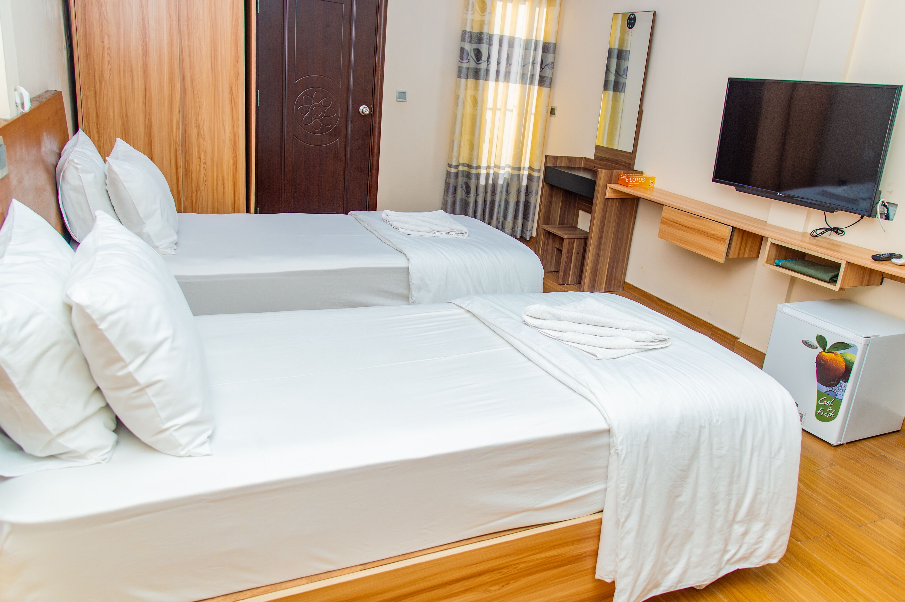 A hotel room with two beds, a TV, a small fridge, and a wooden desk.