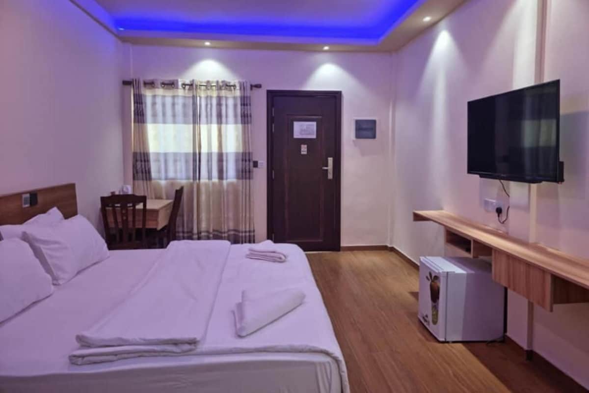 A hotel room with a bed, a desk, a chair, a television, and a small refrigerator.
