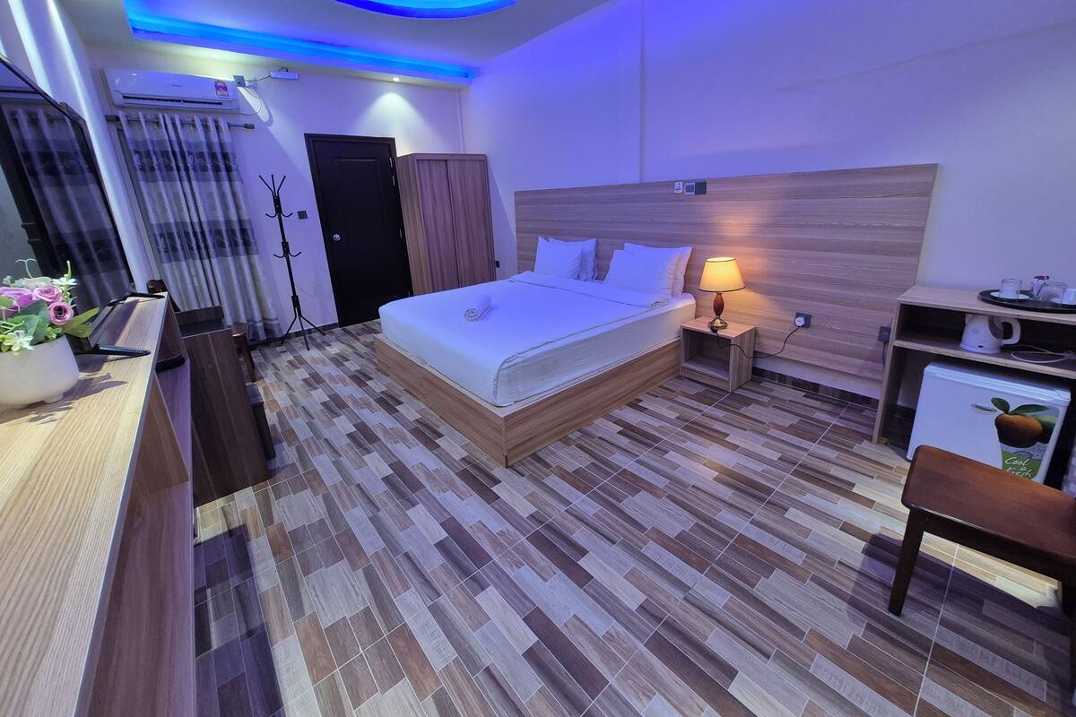 Une chambre d’hôtel moderne avec un lit bien fait, une lampe de chevet, un petit bureau avec une chaise et un réfrigérateur.