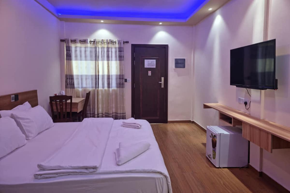 A hotel room with a bed, a desk, a television, and a small refrigerator.