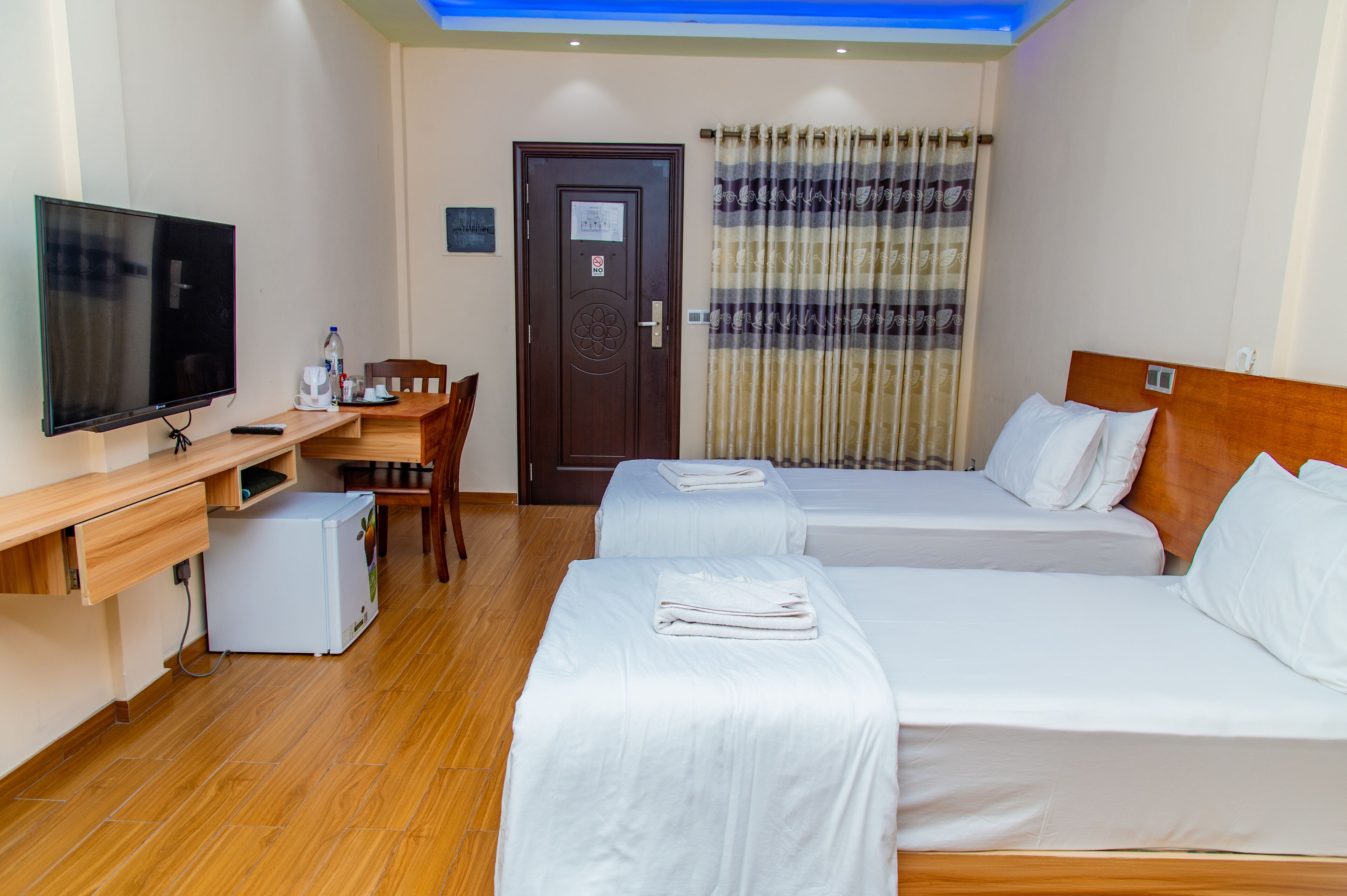 Ett hotellrum med två sängar, ett skrivbord med en tv, ett litet kylskåp och en dörr med en skylt som säger ”Ingen tillträde”.
