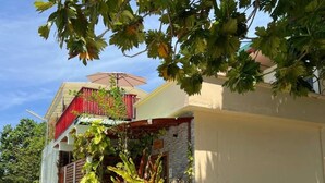 Un edificio de dos pisos con un balcón, un muro de piedra y diversas plantas.