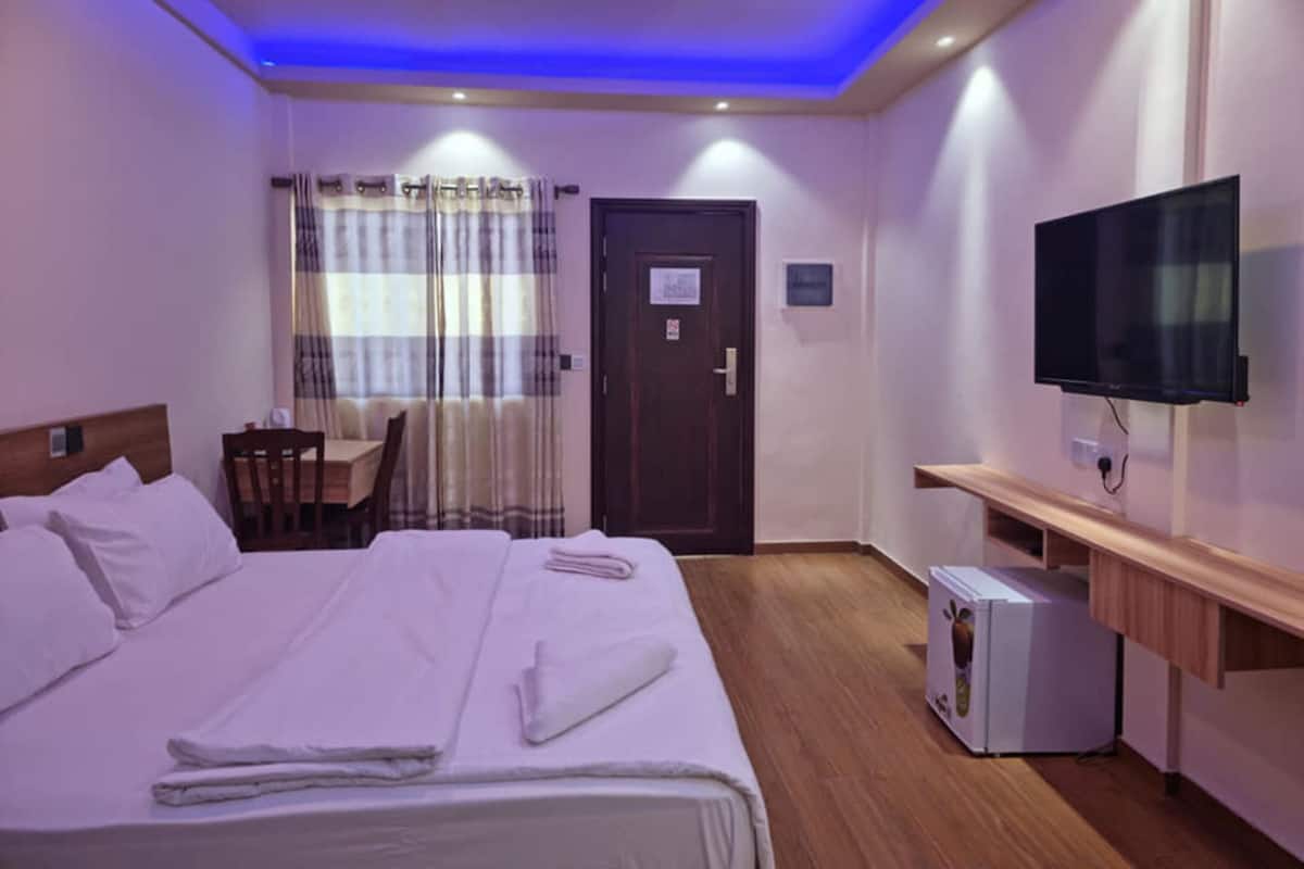 Une chambre d’hôtel équipée d’un lit, d’un bureau, d’une télévision et d’un petit réfrigérateur.