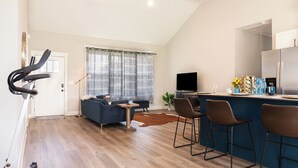 Un grand espace de vie comprenant un tapis de course, un canapé, une table basse et un coin bar avec des tabourets.