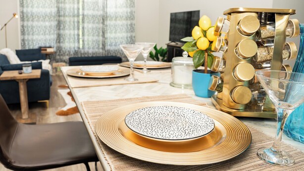 Un coin repas avec une table en bois dressée pour deux personnes, un canapé bleu et une machine à café décorative.