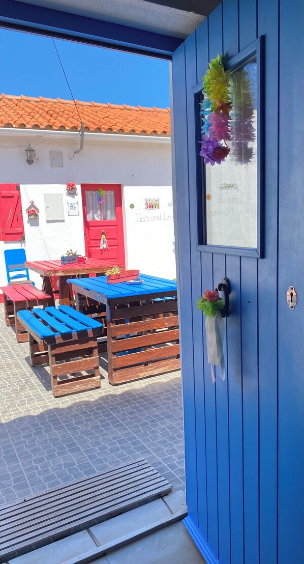 Eine blaue Tür mit Fenster, eine rote Tür und eine weiße Wand mit einem Ziegeldach.