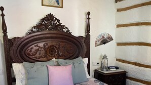 A bedroom with a wooden bed, floral bedding, a nightstand with a lantern, and a wall-mounted fan. - Casal DOS Carpinteiros 4 (Silveira)