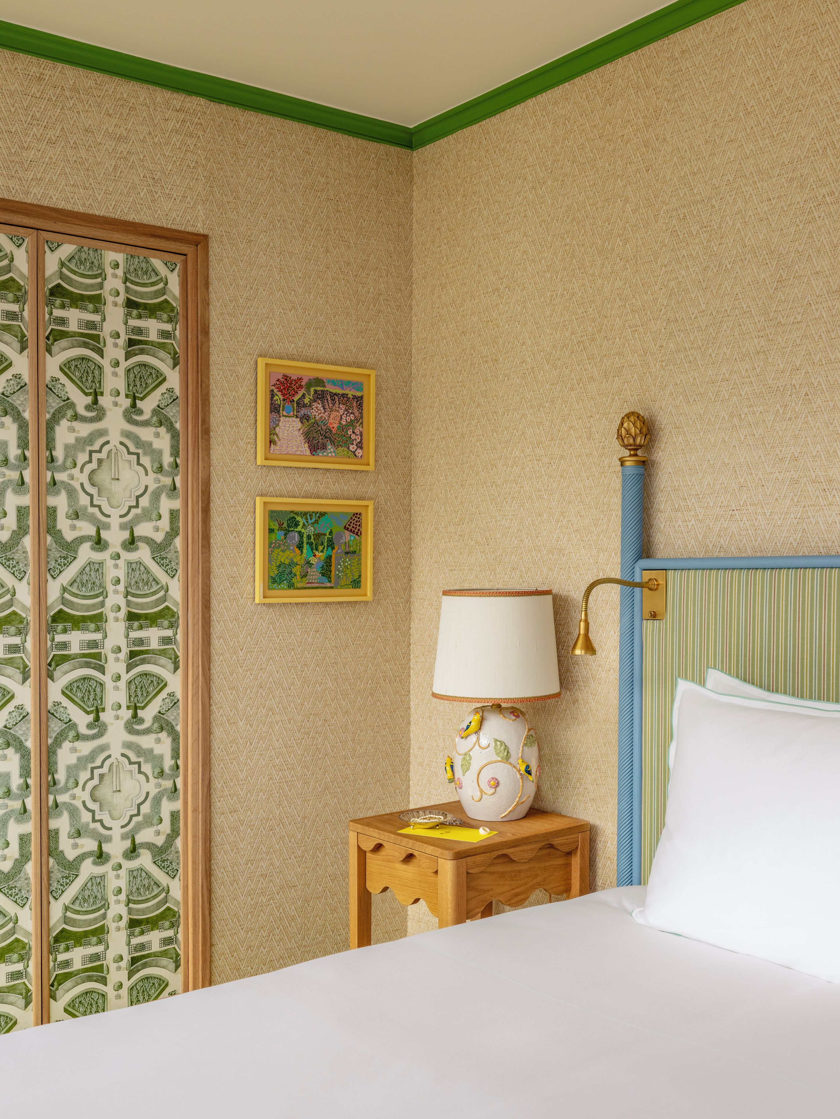 A hotel room with a bed, a nightstand with a lamp, and two framed pictures on the wall.