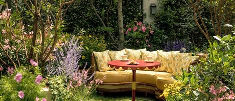 Un jardin avec un canapé jaune et une table rouge, entouré de différentes plantes et fleurs.