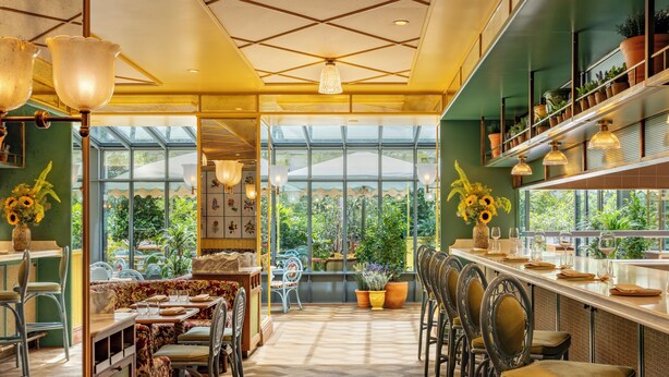 A restaurant with a long counter, multiple chairs, and a view of greenery through large windows. - La Fantaisie (Paris)