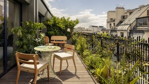 A rooftop terrace with a wooden table and chairs, surrounded by lush greenery and a black metal fence. - La Fantaisie (Paris)