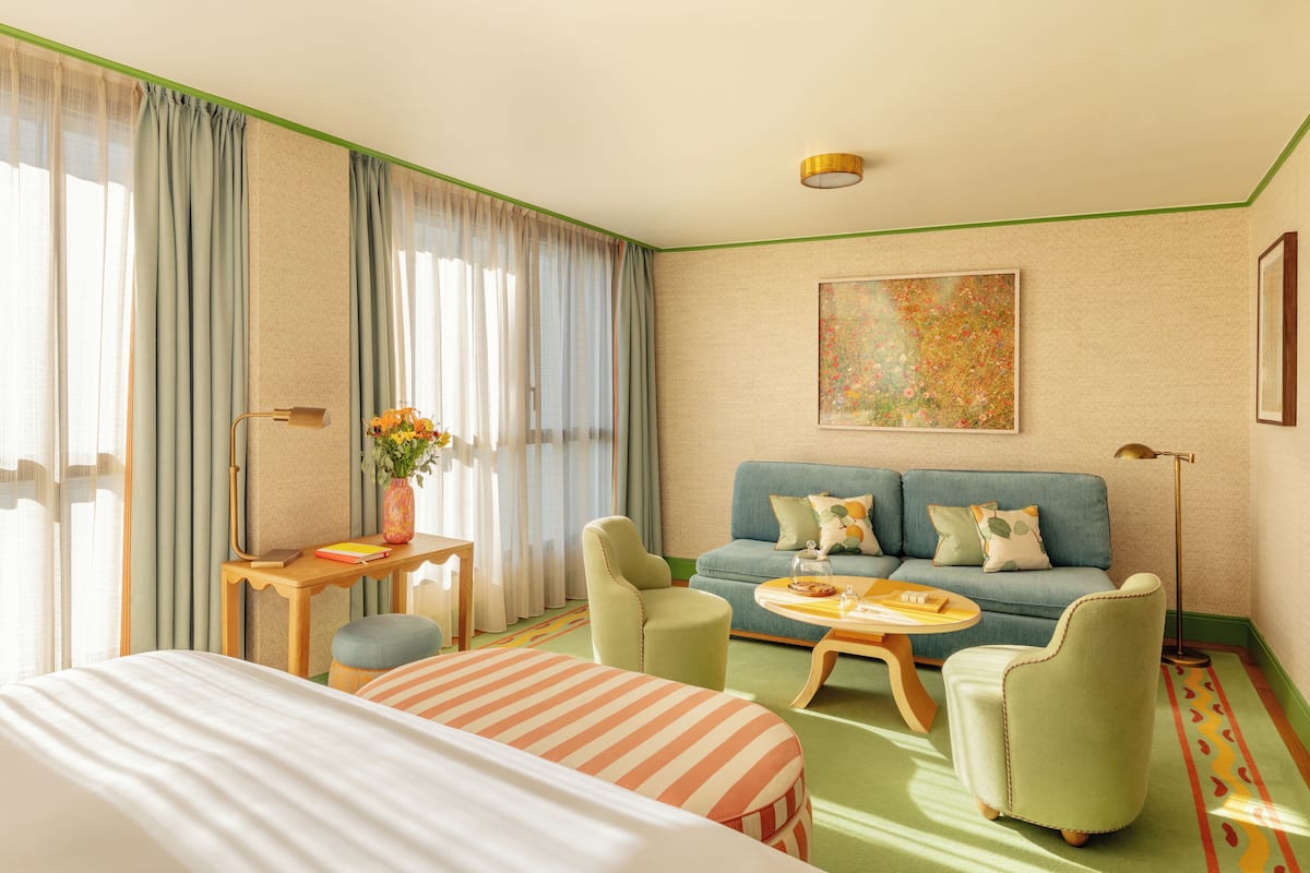 A hotel room with a bed, a sofa, two armchairs, a small table, and a painting on the wall.
