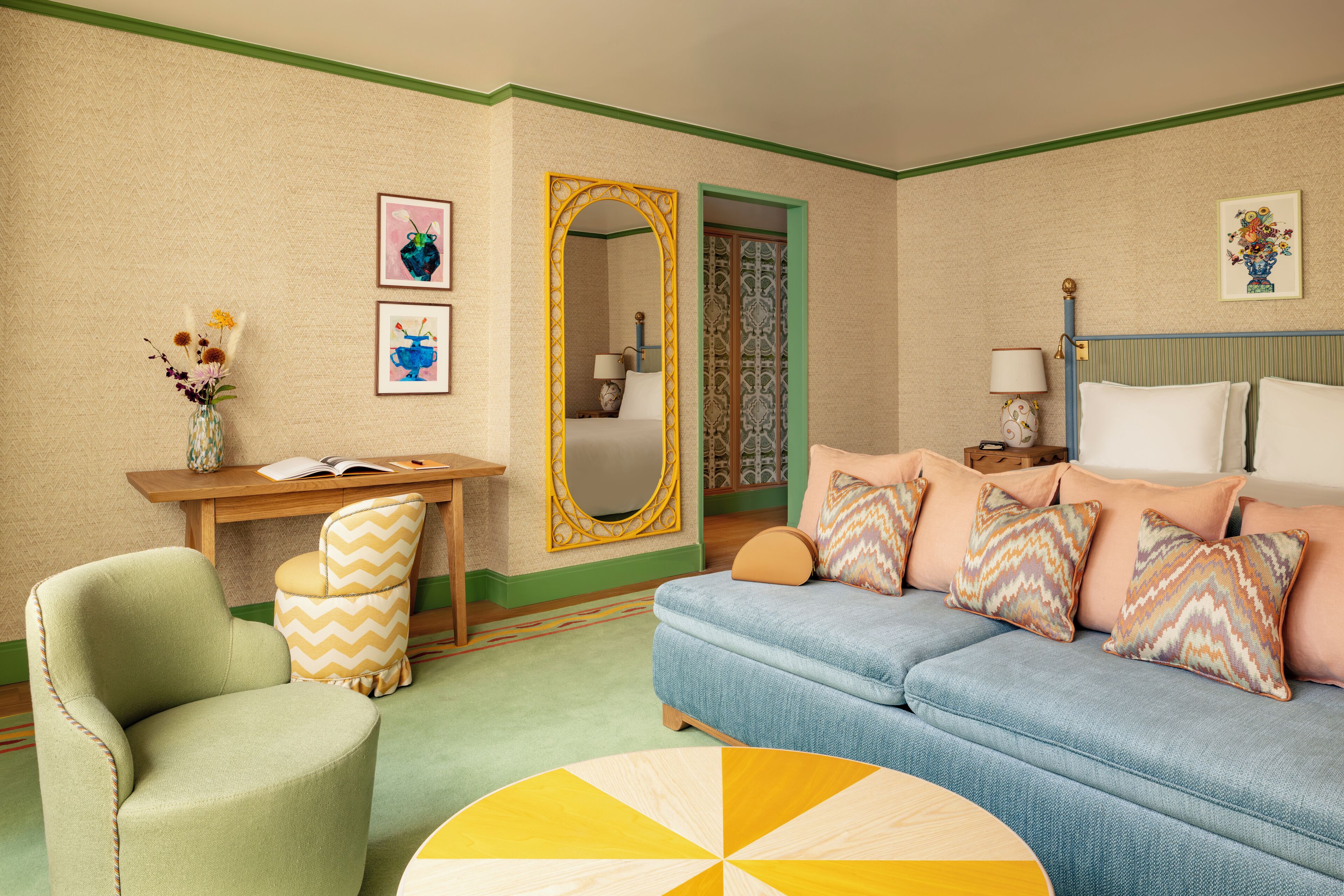 Quarto de hotel aconchegante com esquema de cores verde e bege, apresentando um sofá, uma poltrona, uma mesa redonda e um espelho.