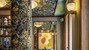 A cozy living room with a large floral-patterned column, a sofa, a coffee table, and a bookshelf filled with books. - La Fantaisie (Paris)