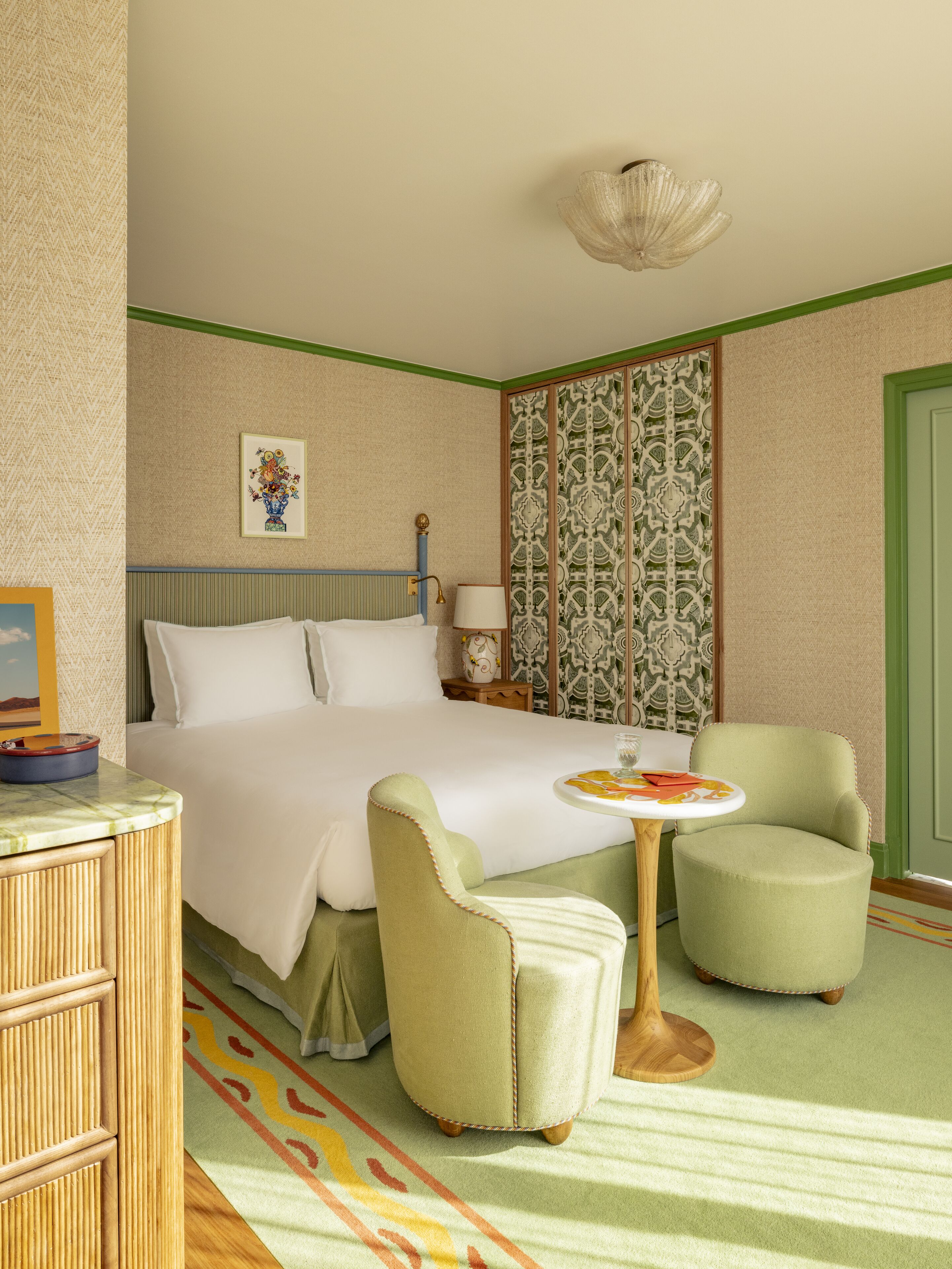 A hotel room with a bed, two armchairs, a small table, and a decorative wall panel.