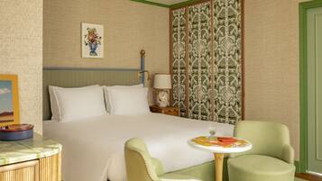 A hotel room with a bed, two armchairs, a small table, and a decorative wall panel.
