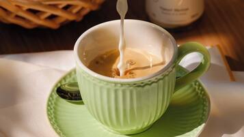 A cup of coffee with milk being poured into it, placed on a green saucer.