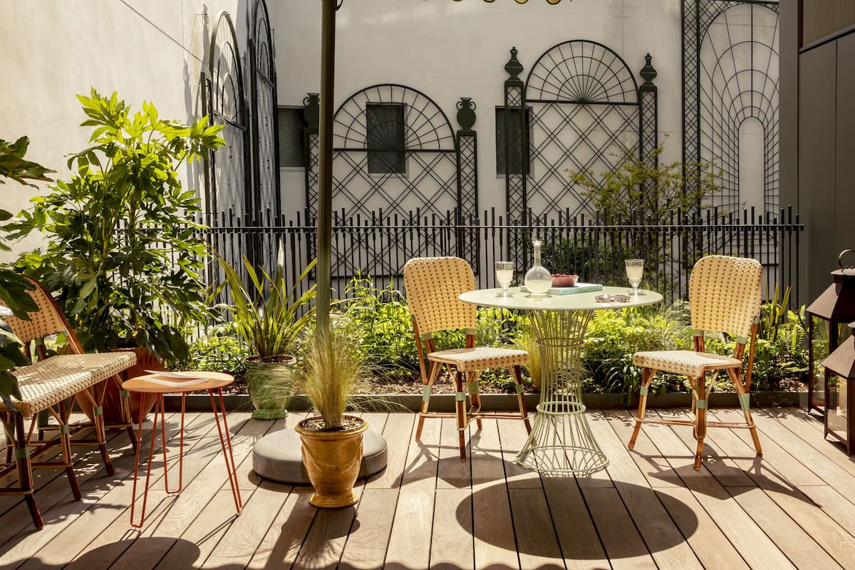 An outdoor patio with wooden flooring, wicker chairs, a table with a glass, and a large umbrella.