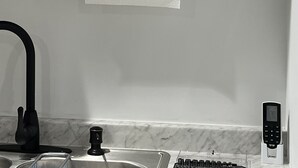 Un bany amb aixeta negra, taulell de marbre, dosificador de tovalloles i estació de càrrega per a telèfon mòbil.