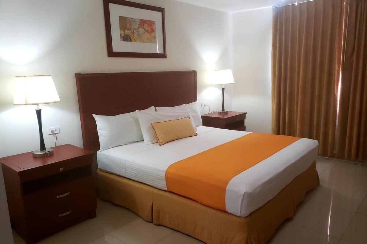 A hotel room with a large bed, two bedside tables with lamps, a framed picture on the wall, and a window with curtains.