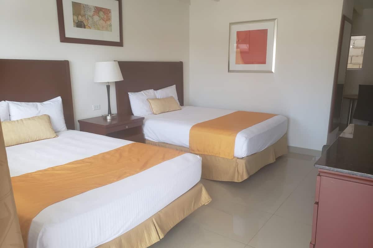 A hotel room with two beds, a nightstand, a lamp, and a television.