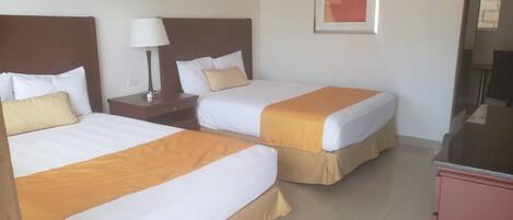 A hotel room with two beds, a nightstand, a lamp, and a television.