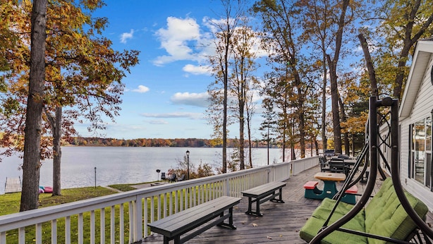Une terrasse en bois, dotée de bancs et d’une chaise suspendue, qui offre une vue sur un lac.