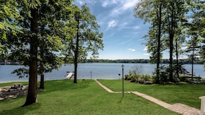 Une zone herbeuse avec un sentier menant à un quai au bord d’un lac, le tout entouré d’arbres.