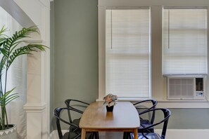 A dining area with a wooden table, two chairs, a potted plant, and a window with blinds.
