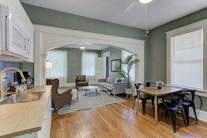 Una cocina moderna con microondas integrado, un lavamanos y una cafetera. Hay una zona de comedor con una mesa y sillas, y una sala de estar con un sofá y una mesa de centro.