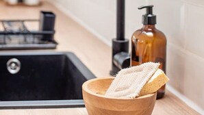 Un lavello da cucina con una ciotola di legno contenente un panno e una bottiglia di sapone.