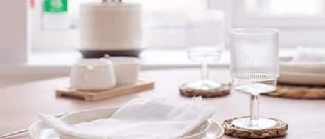 A dining table set with white plates, clear glasses, and a potted plant in the background.