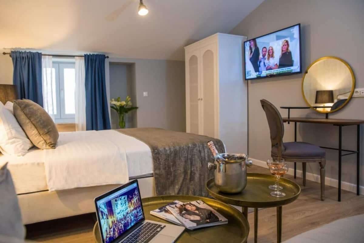 A hotel room with a bed, a desk with a laptop, a television, and a minibar.