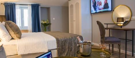A hotel room with a bed, a desk with a laptop, a television, and a minibar.