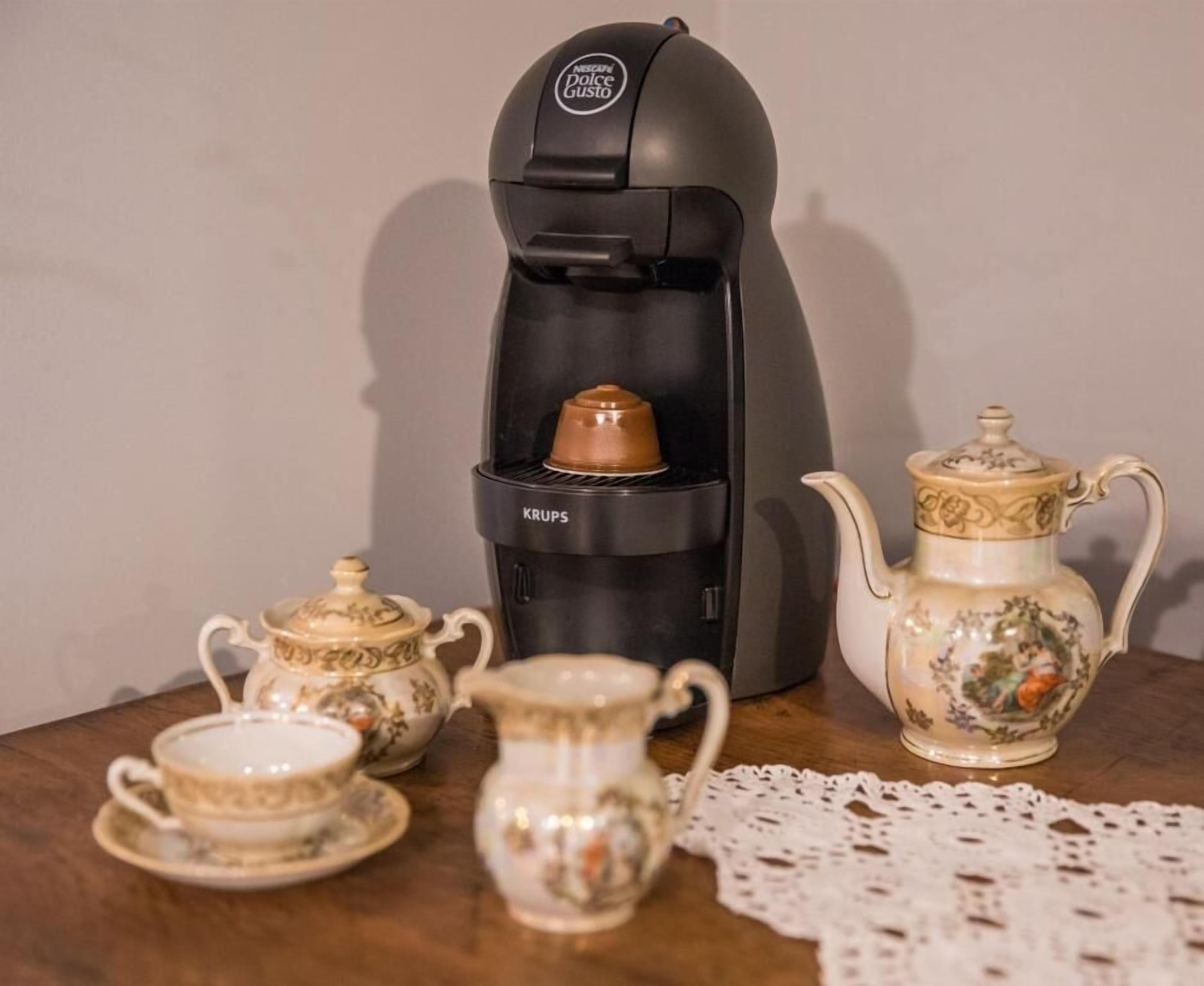 Una moka con marchio KUPS, una teiera e due tazze su un tavolo di legno.