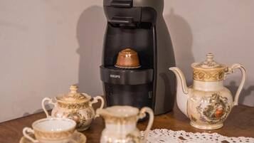 A coffee maker with a KUPS brand, a teapot, and two cups on a wooden table.