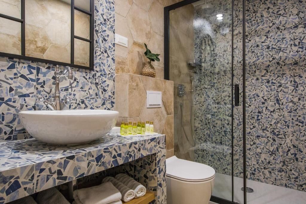 Un baño con un revestimiento de mosaicos, un lavamanos tipo recipiente, una cabina de ducha de vidrio y un inodoro.