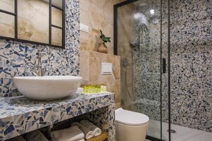 Un baño con un revestimiento de mosaicos, un lavamanos tipo recipiente, una cabina de ducha de vidrio y un inodoro.