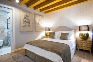 Quarto com teto de madeira, cama com roupa branca, duas luminárias na parede e mesa de cabeceira com uma tigela decorativa.