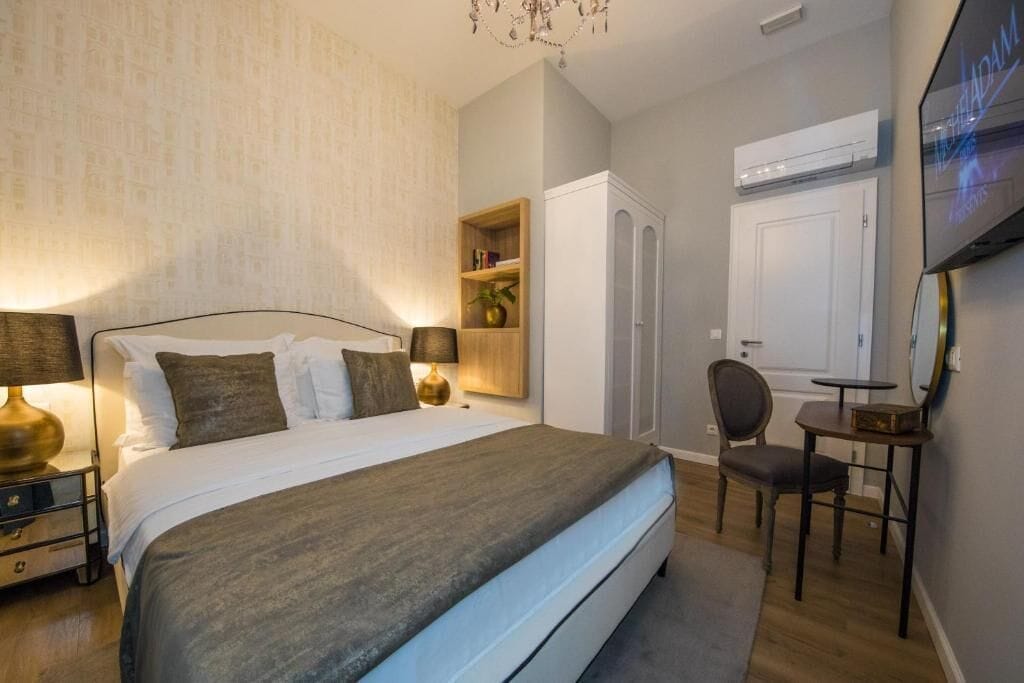 A bedroom with a bed, bedside tables, a desk, a chair, a wardrobe, and a television.