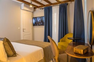 Quarto de hotel com uma cama, uma cadeira amarela, uma mesa redonda pequena e uma TV na parede.