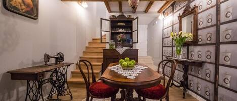 Un comedor con una mesa de madera, sillas tapizadas en rojo, un mantel de encaje y una escalera que lleva a otra habitación.