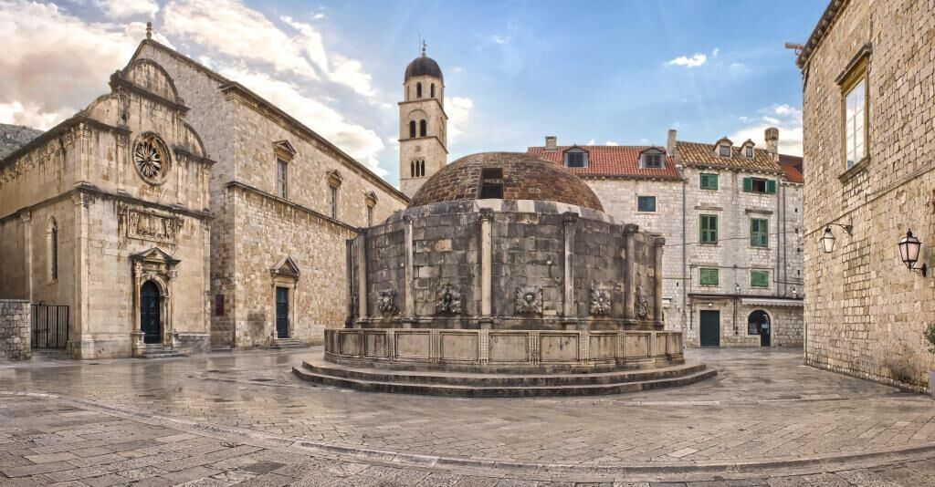 A historic square with a central fountain, a church, and a tower.