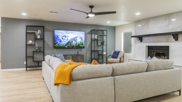 A modern living room with a grey sofa, a flat-screen TV, a fireplace, and a ceiling fan. - Cozy house w/ putting green, mtn. views, BBQ (Fountain Hills)