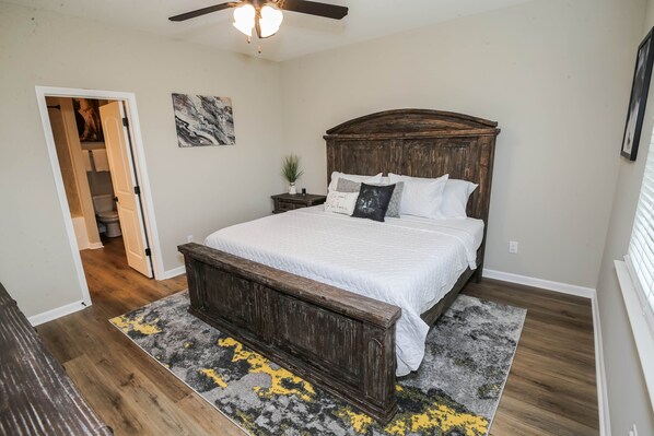 A bedroom with a wooden bed, a ceiling fan, a nightstand with a plant, and a door leading to another room.