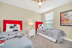 A bedroom with two beds, each with Mickey Mouse-themed bedding, a nightstand with a lamp, and a ceiling fan. - 5BR | 3 Ensuites | FREE Water Park Near Disney (Champions Gate)