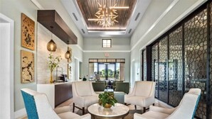 A modern lobby with a reception desk, two seating areas with chairs, a decorative ceiling, and a view through a large window. - Water Park included. Spa & Golf Resort Near Disney! (Champions Gate)
