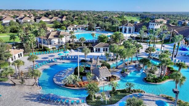 A resort with multiple swimming pools, palm trees, and a golf course in the background. - Water Park included. Spa & Golf Resort Near Disney! (Champions Gate)